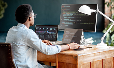 person coding at desk with multiple monitors
